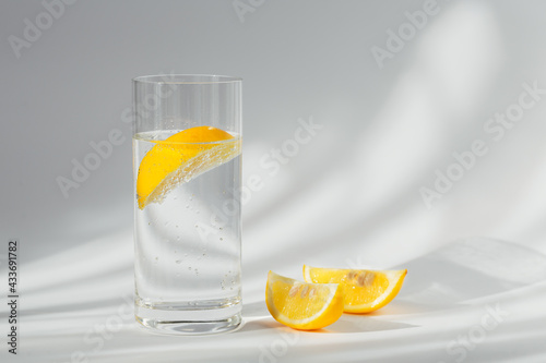 Glass of clean mineral sparkling water with ice and lemon on a white background with sunshine