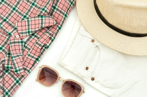 summer flat lay: shirt with a pink check pattern, sunglasses, white jeans and a woman's hat