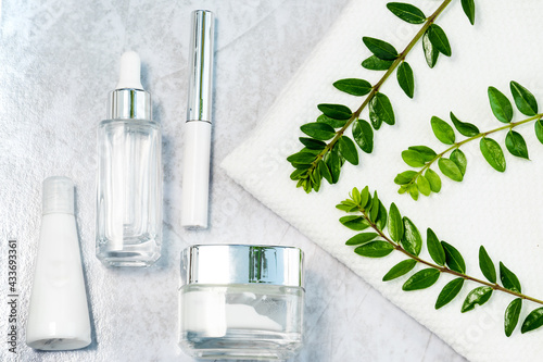 cosmetically flat lay: jars of skin care cosmetics in silver colour, white towel and a sprig of luscious greenery photo