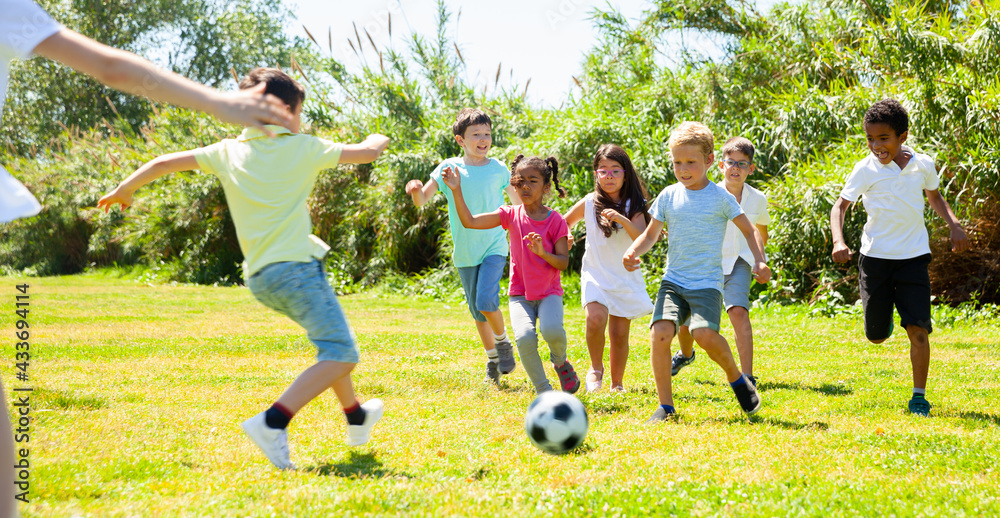 Obraz premium Company of glad children playing football on the playground in park. High quality photo