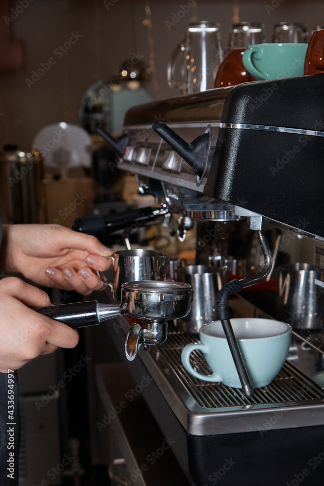 barista prepares and pours coffee into a mug on the coffee machine, close-up, hands of a woman, blurred background