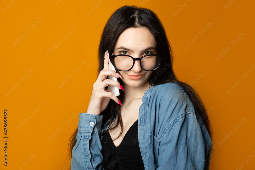 portrait of a beautiful cute woman with glasses on a yellow background with a phone portrait of a beautiful cute woman with glasses on a yellow background with a phone