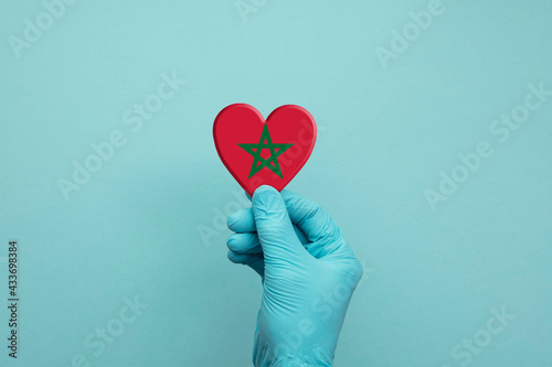 Hands wearing protective surgical gloves holding Morocco flag heart