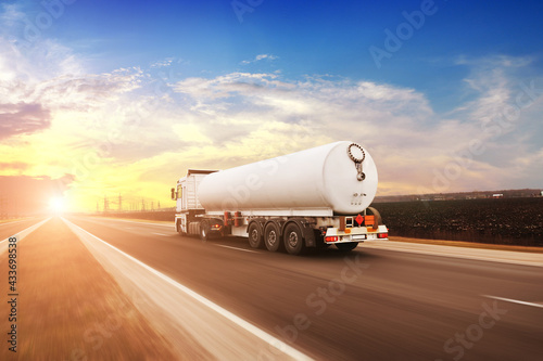 Big fuel tanker truck driving fast on a countryside road against a sky with a sunset photo
