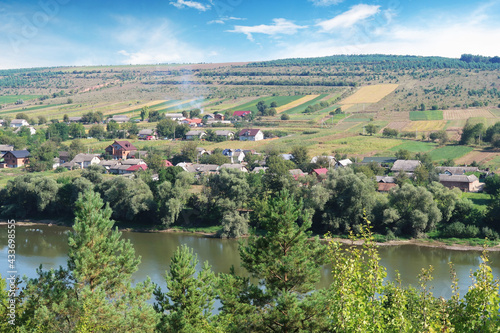 Aerial view of a valley with a village and fields on a hill with a river against a sky with clouds