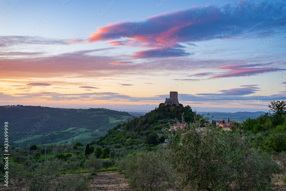 Rocca d'Oria, a medieval village and fortress in Orcia Valley, Tuscany, Italy. Unique view at dusk, the stone tower perched on rock cliff against dramatic sky.