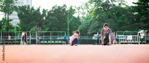 Exercise and relaxing time with family concept. Mom and daughter make gestures start to run a race on running track. Active kid look at camera. Mother playing with cute little girl aged 4 years old.