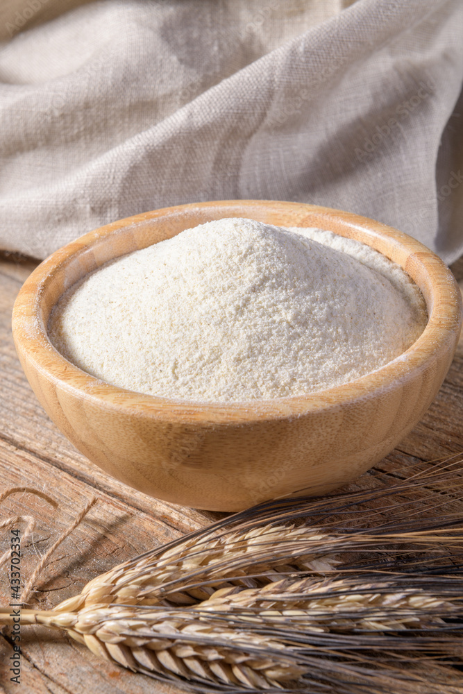 Whole wheat durum flour in wooden bowl with spikelets on a natural wooden background, close up Whole wheat durum flour in wooden bowl with spikelets on a natural wooden background, close up