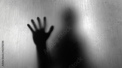 Blurry silhouette of person touching dirty water stained glass with hand