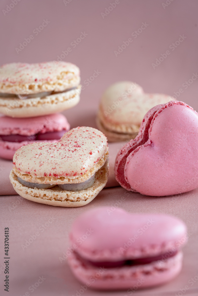 A group of heart-shaped French macaron cookies, vanilla and strawberry flavour, copy space on a pink fabric background