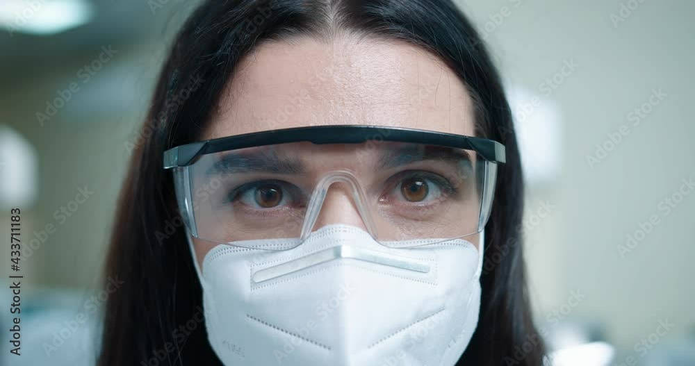 Close up shot of happy young beautiful Caucasian woman medical scientist in protective mask and goggles looking at camera indoor. Medicine, lab scientist, clinical laboratory, doctor job Close up shot of happy young beautiful Caucasian woman medical scientist in protective mask and goggles looking at camera indoor. Medicine, lab scientist, clinical laboratory, doctor job