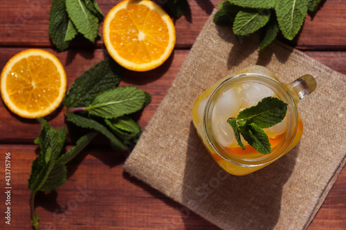 Fresh homemade citrus lemonade in jar with ice, mint and oranges on a wooden table. Summer refreshments. Close-up, selective focus, top view. Hard light