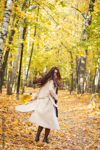 Brunette woman in autumn park and autumn leaves. Small black bag. Autumn mood. Yellow  red and green leaves. Beige coat.