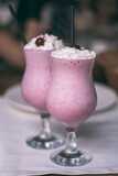 Partially blurred glasses with berry milkshake with straws, whipped cream and cocktail cherries. Vertical