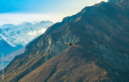 a small plane flying along the mountains of Alaska dwarfed by the size of the mountain.