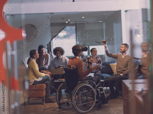 Disabled businessman in a wheelchair at work in modern open space coworking office with team using virtual reality googles drone assistance simulation