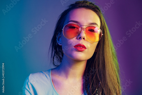 Asian girl in sunglasses and black leather jacket posing against dark blue background