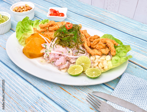 Peruvian food: fish ceviche and chicharron de pescado with fried cassava, sweet corn and sweet potato, served on a white plate photo