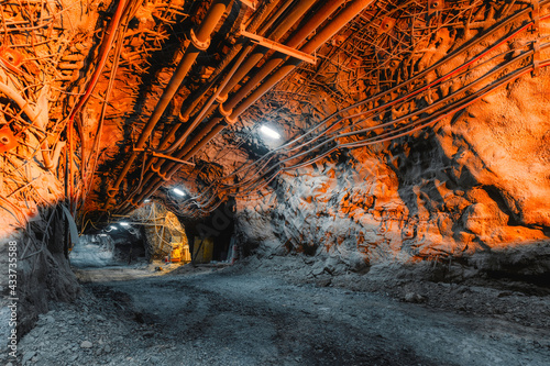 Tunnel of the mining of an underground mine. Lots of pipelines on the ceiling and rail track for trolleys