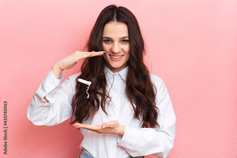 A studio shot of a girl holding a tampon in her hand in a menstrual applicator. Space for the text. The concept of feminine hygiene. A studio shot of a girl holding a tampon in her hand in a menstrual applicator. Space for the text. The concept of feminine hygiene.