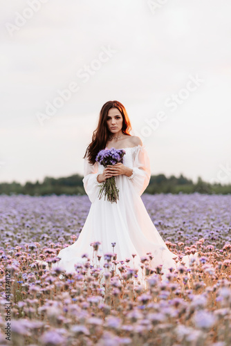 A beautiful girl in a white dress in a blooming field of Provence in a romantic atmosphere with a bouquet in her hands
