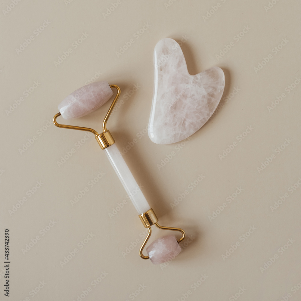 Flatlay of gua sha massage roller and stone scraper tool on neutral ...
