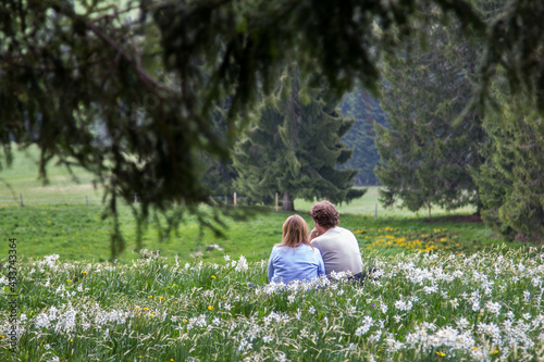 Unidentifiable young couple sitting among blooming field with wild narcissus flower (narcissus poeticus) at the Swiss Alps in vaud riviera over Geneva Lake © Yü Lan