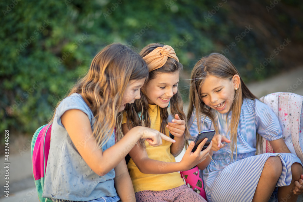 Three little school girls using smart phone together.