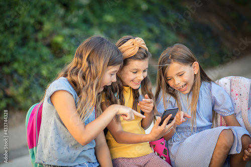 Three little school girls using smart phone together.