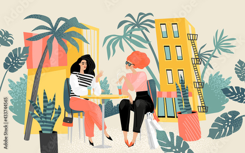Two lovely girls sitting at a table in a summer cafe and chatting. City life