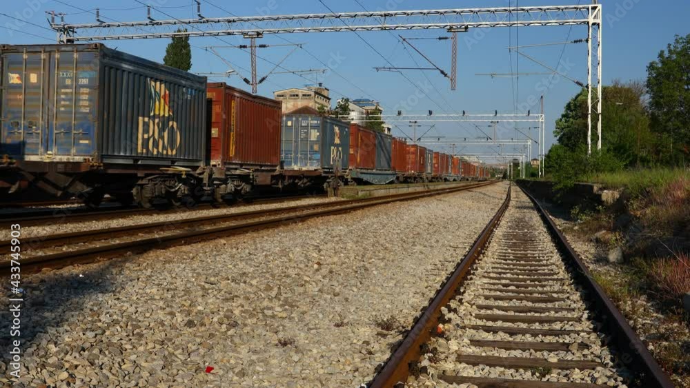 View on long composition, railway freight train of cargo shipping containers in passing through industrial rural place.