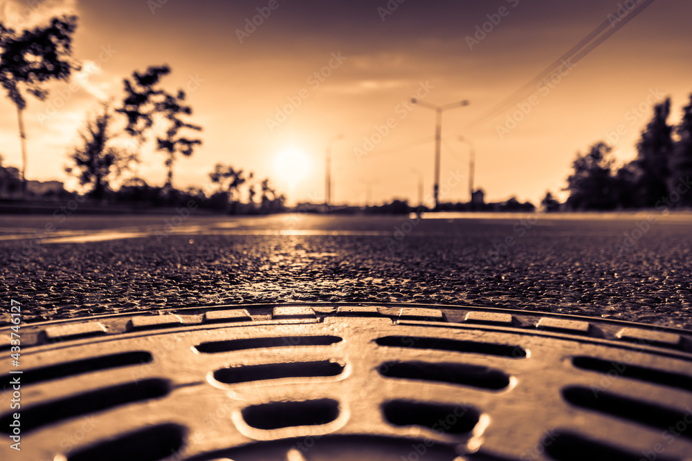 Sunset in the country, the empty highway. Wide angle view of a close up from the level of the sewer manhole on pavement