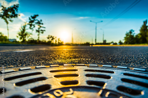 Sunset in the country, the empty highway. Wide angle view of a close up from the level of the sewer manhole on pavement