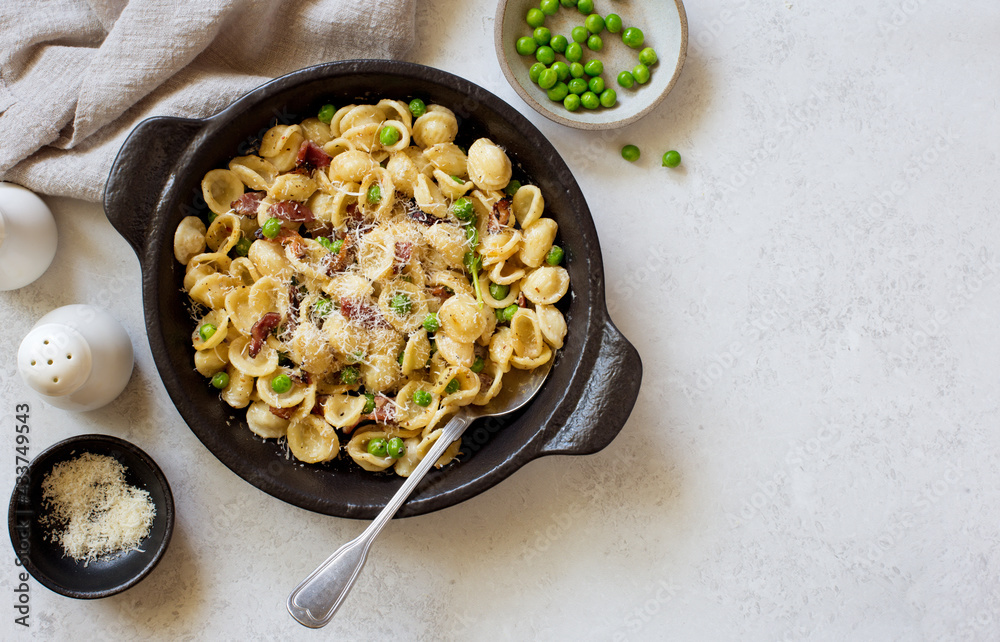 Pasta with fried bacon, green peas and parmesan cheese in rustic cooking pan
