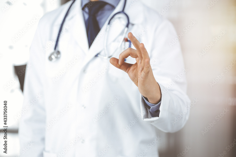 Unknown male doctor standing straight with OK sign in sunny clinic, closeup. Perfect medical service in hospital. Medicine and healthcare concept Unknown male doctor standing straight with OK sign in sunny clinic, closeup. Perfect medical service in hospital. Medicine and healthcare concept