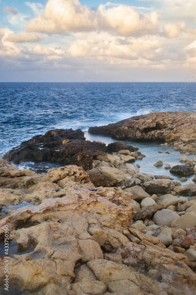 Rocks leading out to the blue ocean water in Qawra, Malta on a fall evening.
