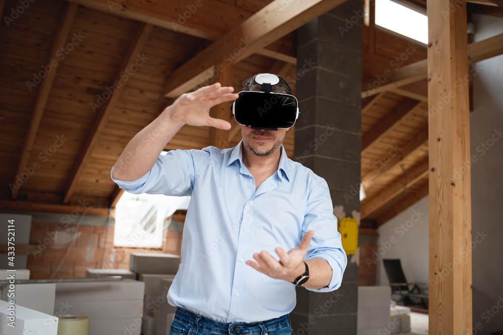 good looking male architect with virtual reality goggles and blue shirt on construction site in loft, attic good looking male architect with virtual reality goggles and blue shirt on construction site in loft, attic
