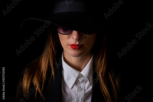 portrait of a beautiful young woman in a black hat and glasses on a black background © Alex