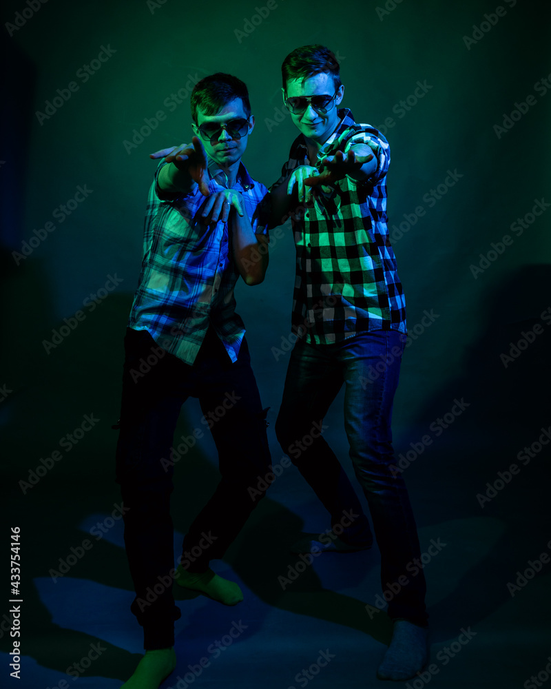Two young men in plaid shirts dance in the studio with multicolored light