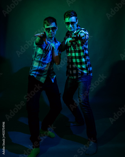 Two young men in plaid shirts dance in the studio with multicolored light