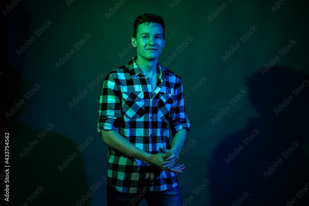 A young man in a studio on a dark background with a multicolored light A young man in a studio on a dark background with a multicolored light