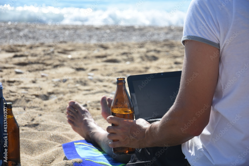 Man drink beer and work on laptop on the beach. Traveler enjoy on send with netbook and cold beer