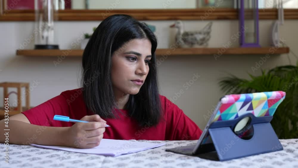 Focused Asian woman in using pc tablet sit at table at home, pretty student girl writes notes learn language, do task, watch on-line webinar, e-learn education concept. work from home concept.
