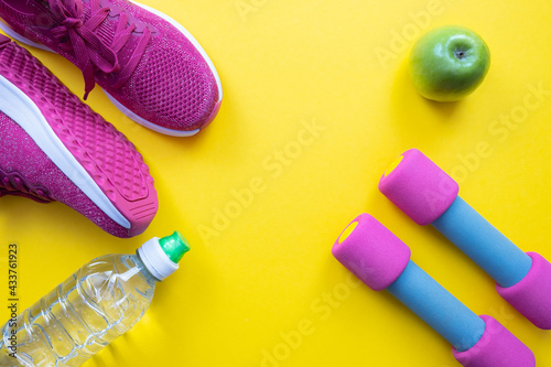pink sneakers and dumbbells in the corners, a green apple and a bottle of water