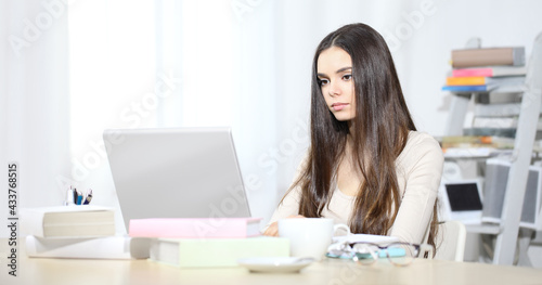 Young woman sitting at desk in office room and working on her laptop