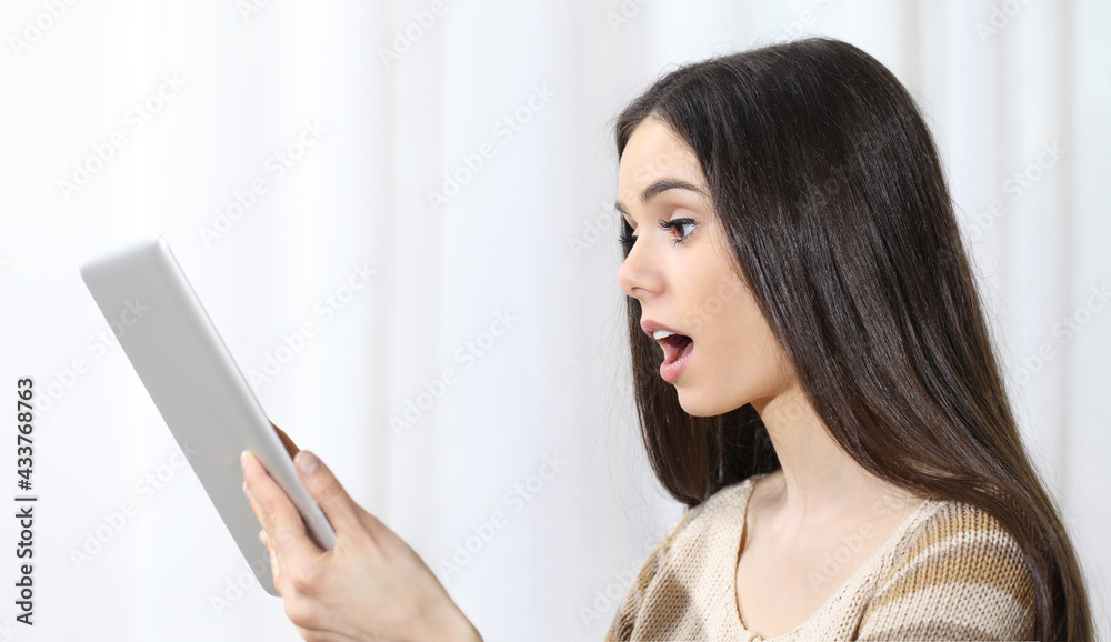 Young woman holding a tablet and looking at it surprised with her mouth open on white background Young woman holding a tablet and looking at it surprised with her mouth open on white background