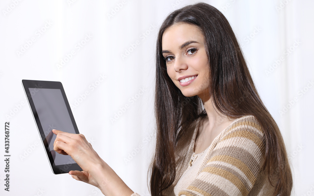 Young woman holding a tablet and pointing finger at screen while looking at camera smiling on white background Young woman holding a tablet and pointing finger at screen while looking at camera smiling on white background
