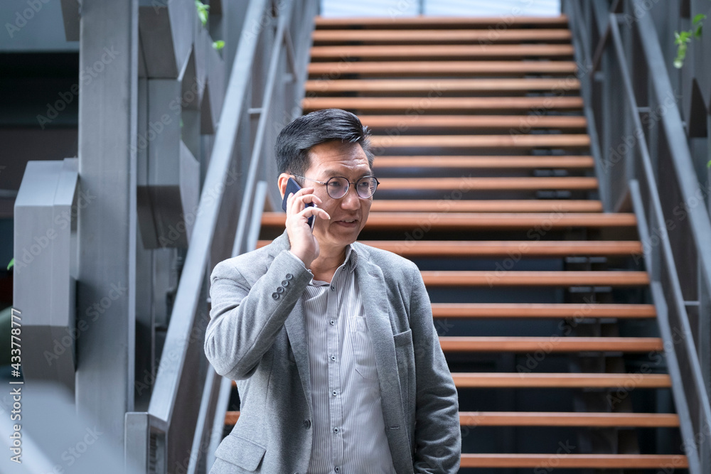Asian businessman holding phone to his ears, talking or chatting. Staircase at the background. Asian businessman holding phone to his ears, talking or chatting. Staircase at the background.