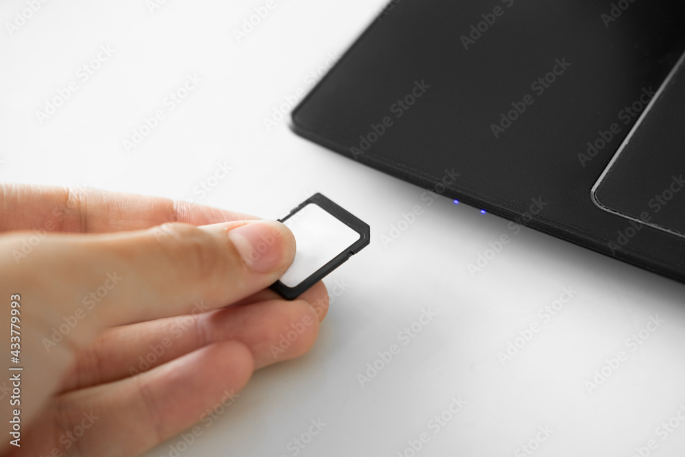 A human hand inserts an SD memory card into a personal laptop computer. A human hand inserts an SD memory card into a personal laptop computer.
