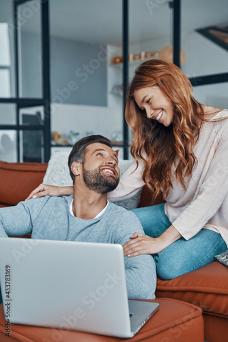 Loving young couple using laptop and smiling while spending time at home